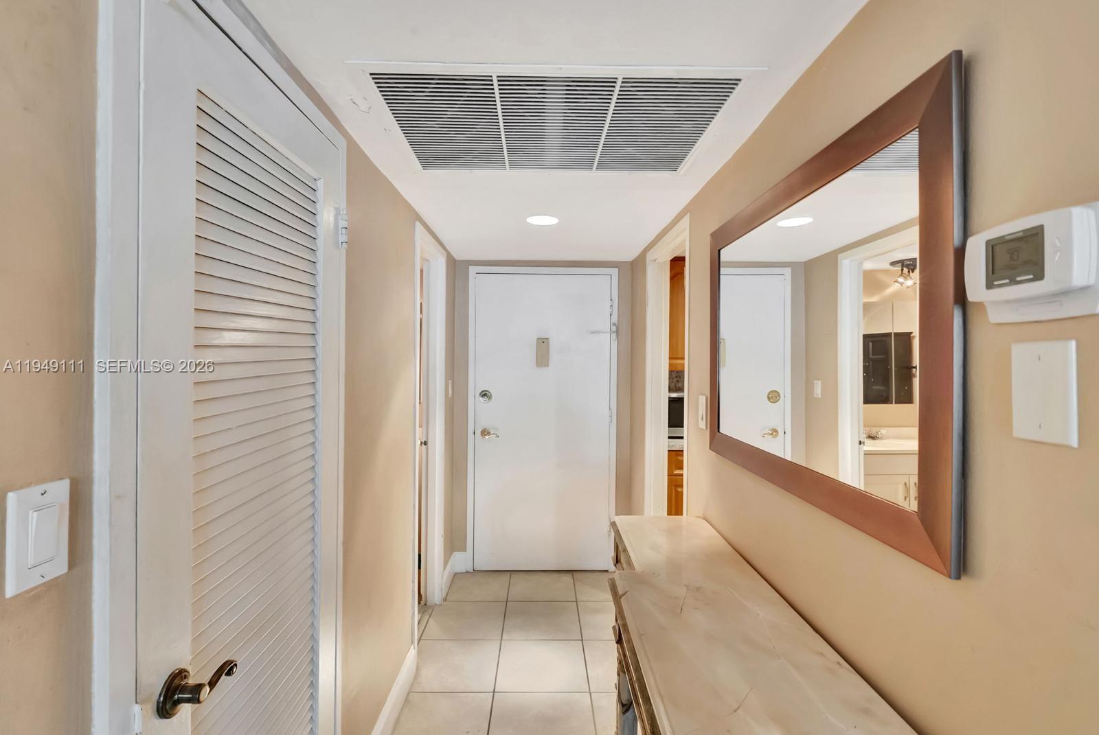A hallway features beige walls, tile flooring, a louvered closet door, and a wall mirror — 5401 Collins Ave # 340, Miami Beach FL 33140, MIAMI BEACH, FL