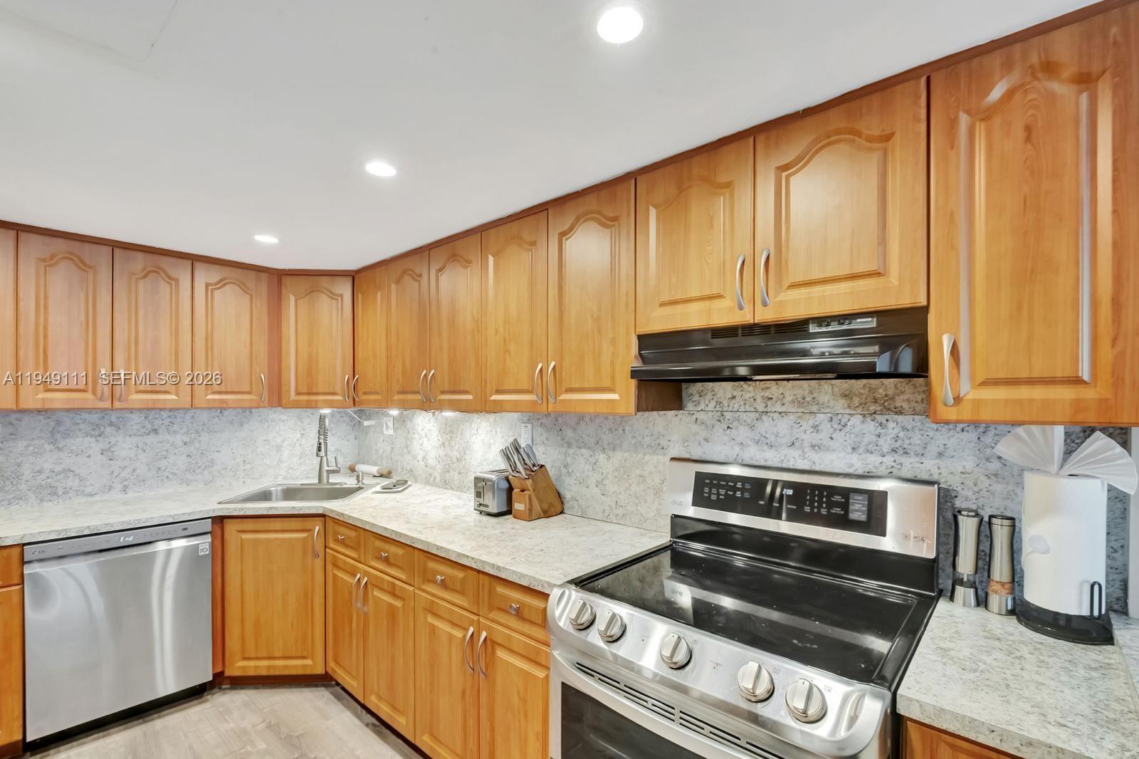 A kitchen features wood cabinets, stainless steel appliances, and light-colored granite countertops — 5401 Collins Ave # 340, Miami Beach FL 33140, MIAMI BEACH, FL