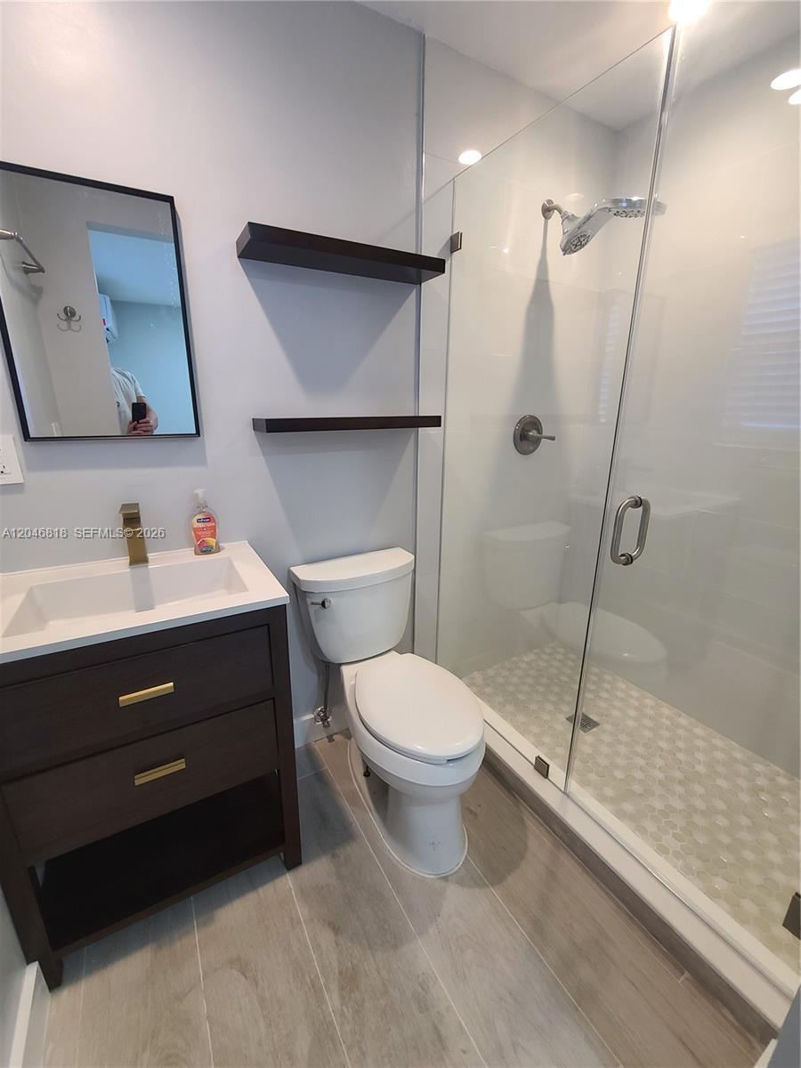 A modern bathroom features a dark wood vanity, floating shelves, a toilet, and a glass shower — 321 Hayes St # 3, Hollywood FL 33019, HOLLYWOOD, FL