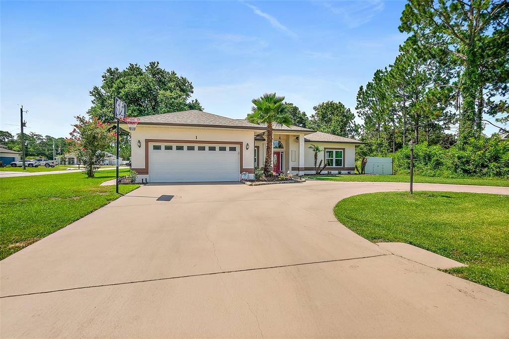 A single-story house with a large concrete driveway, a two-car garage, and a palm tree — 1 SLIPPER FLOWER PATH E, PALM COAST, FL