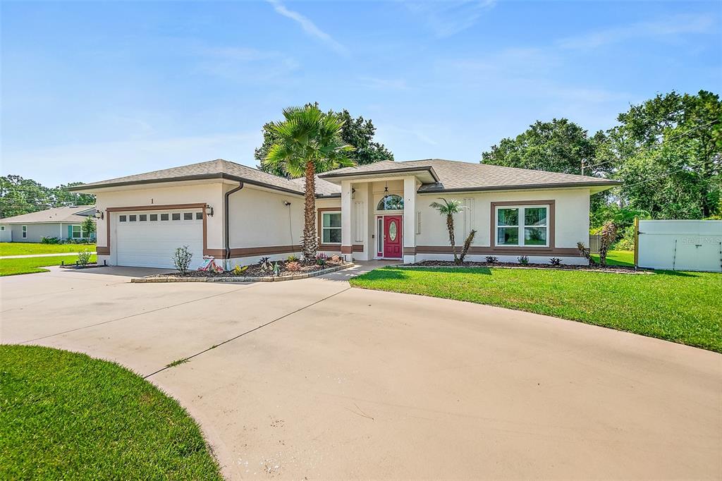 A single-story house with a beige stucco exterior, a two-car garage, and a red front door — 1 SLIPPER FLOWER PATH E, PALM COAST, FL