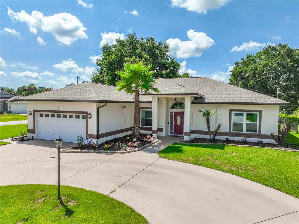 A single-story house with a white stucco exterior, a two-car garage, and a palm tree — 1 SLIPPER FLOWER PATH E, PALM COAST, FL
