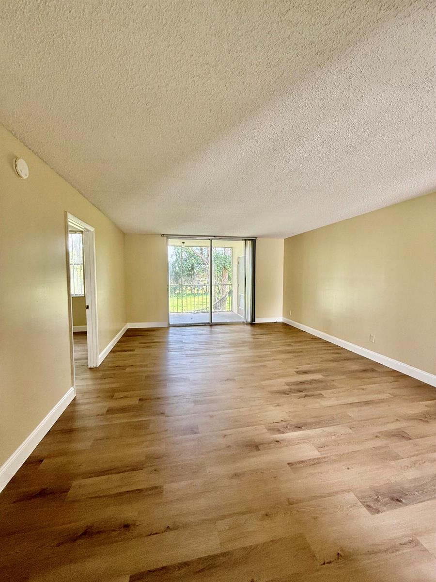 An empty living room features light-colored walls, wood-look flooring, and a sliding glass door — 7895 Margate Boulevard # 203, Margate FL 33063, MARGATE, FL