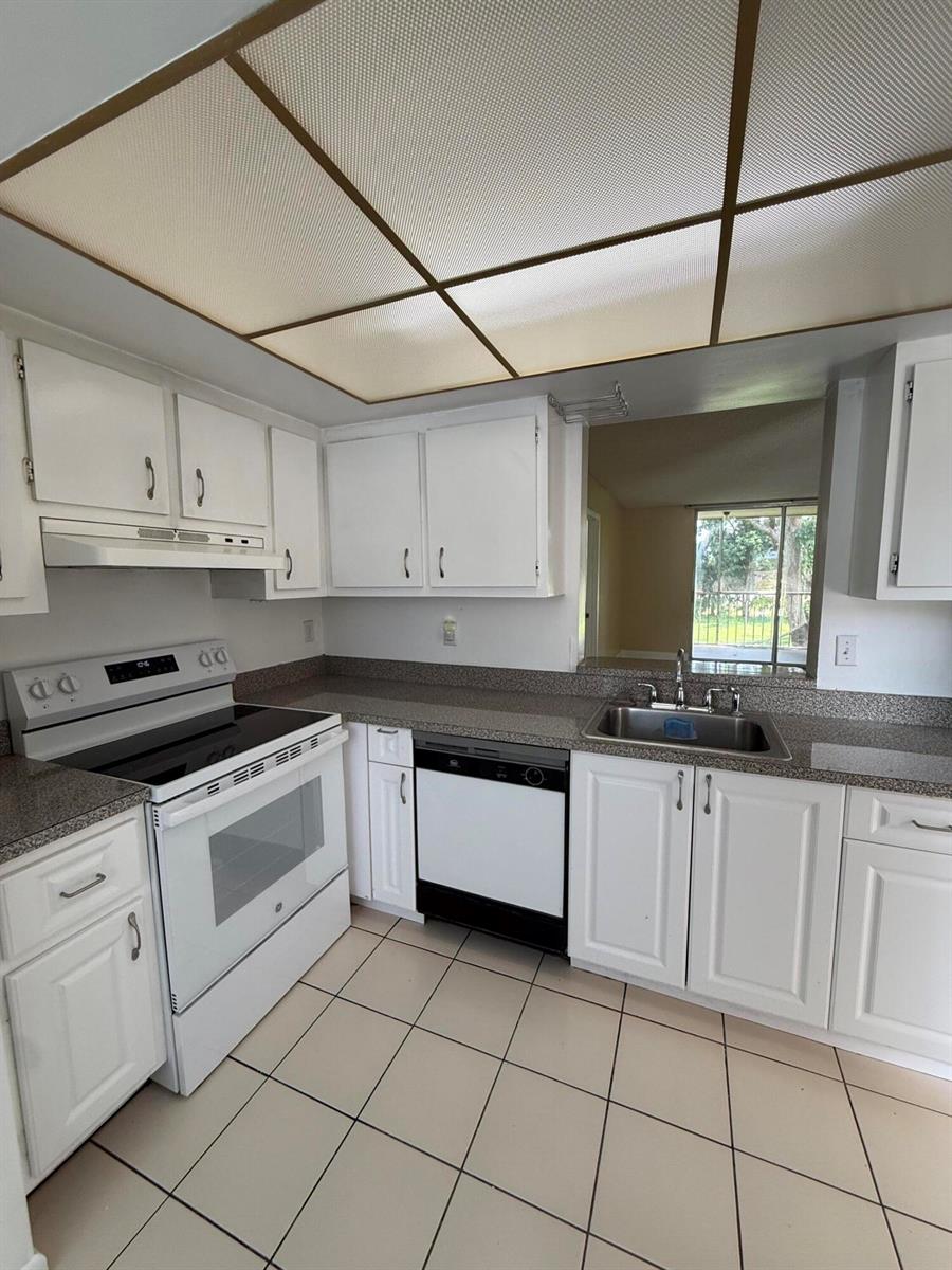 A kitchen with white cabinets, a white stove, a dishwasher, and tan tile flooring — 7895 Margate Boulevard # 203, Margate FL 33063, MARGATE, FL