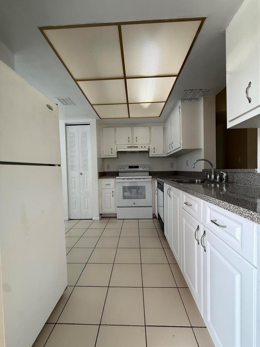 A galley kitchen features white cabinets, granite countertops, tile flooring, and a drop ceiling — 7895 Margate Boulevard # 203, Margate FL 33063, MARGATE, FL