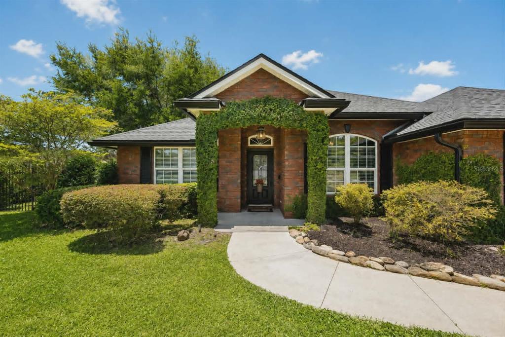 A brick house exterior features a front entrance framed by a green vine-covered archway — 96095 GRAVEL CREEK DRIVE, YULEE, FL
