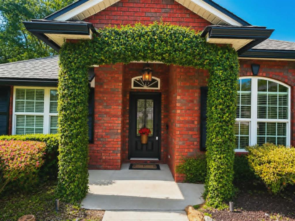 The front entrance of a brick house features a vine-covered archway and a black door — 96095 GRAVEL CREEK DRIVE, YULEE, FL