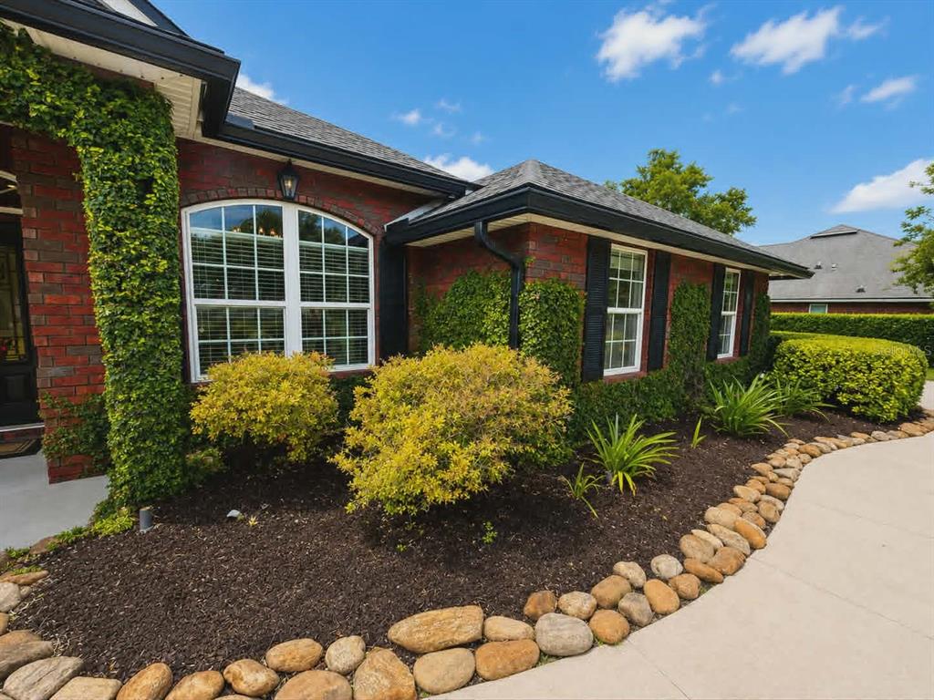A brick house exterior features a curved stone-bordered garden bed with shrubs and ivy — 96095 GRAVEL CREEK DRIVE, YULEE, FL