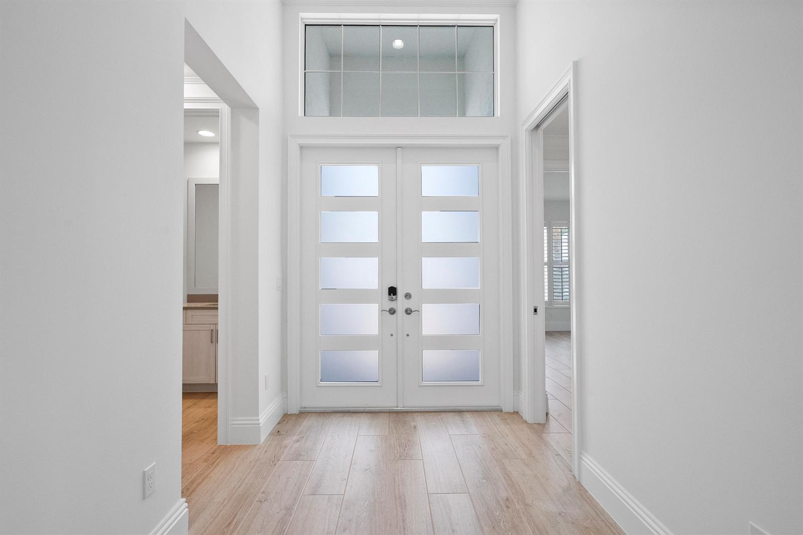 A bright entryway features double glass-paneled doors, a transom window, and light wood-look flooring — 4226 Lucaya Pointe Way, Vero Beach FL 32967, VERO BEACH, FL