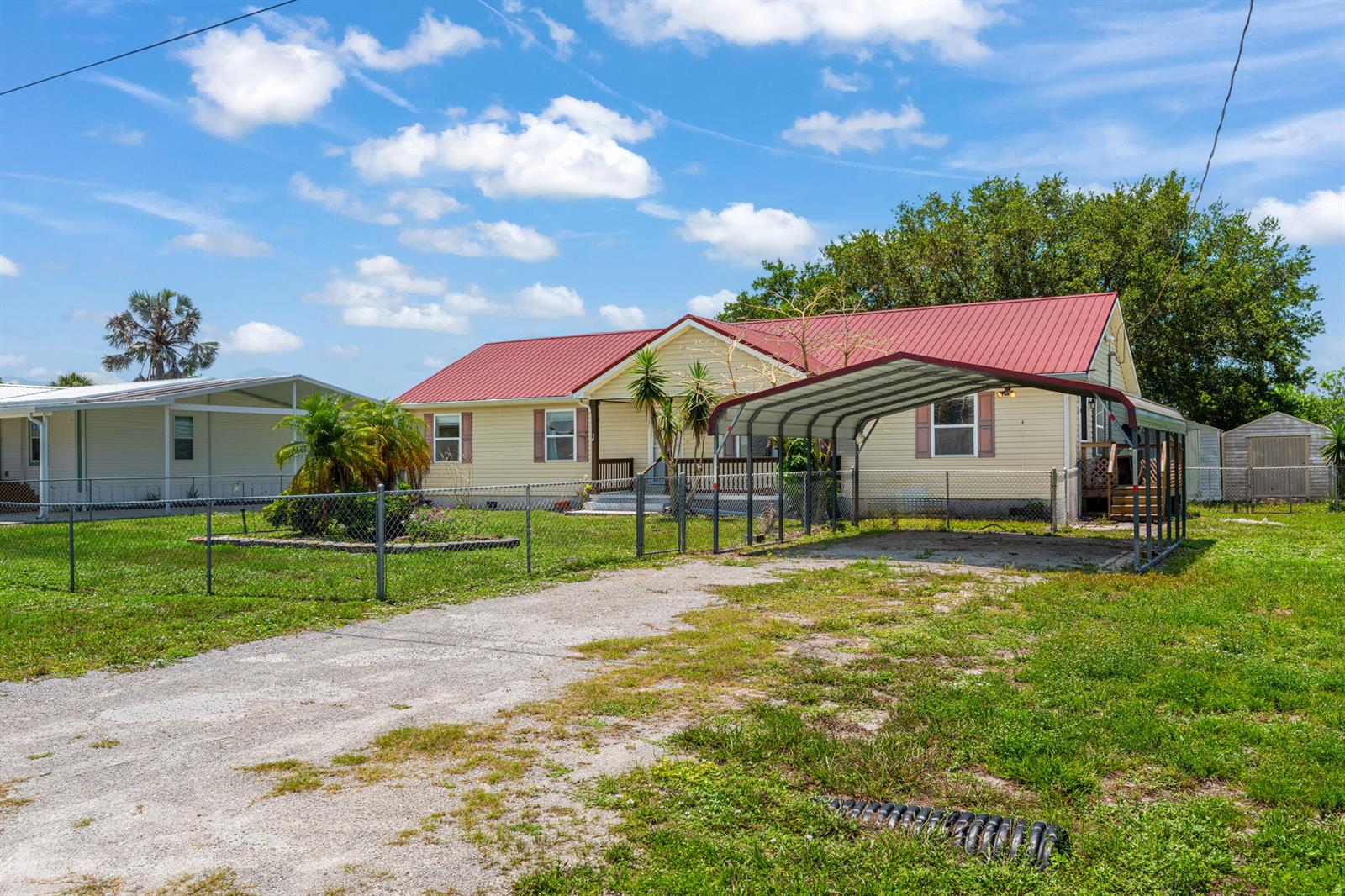 A yellow house with a red metal roof and a metal carport stands on grass — 2546 SE 27th Street, Okeechobee FL 34974, OKEECHOBEE, FL