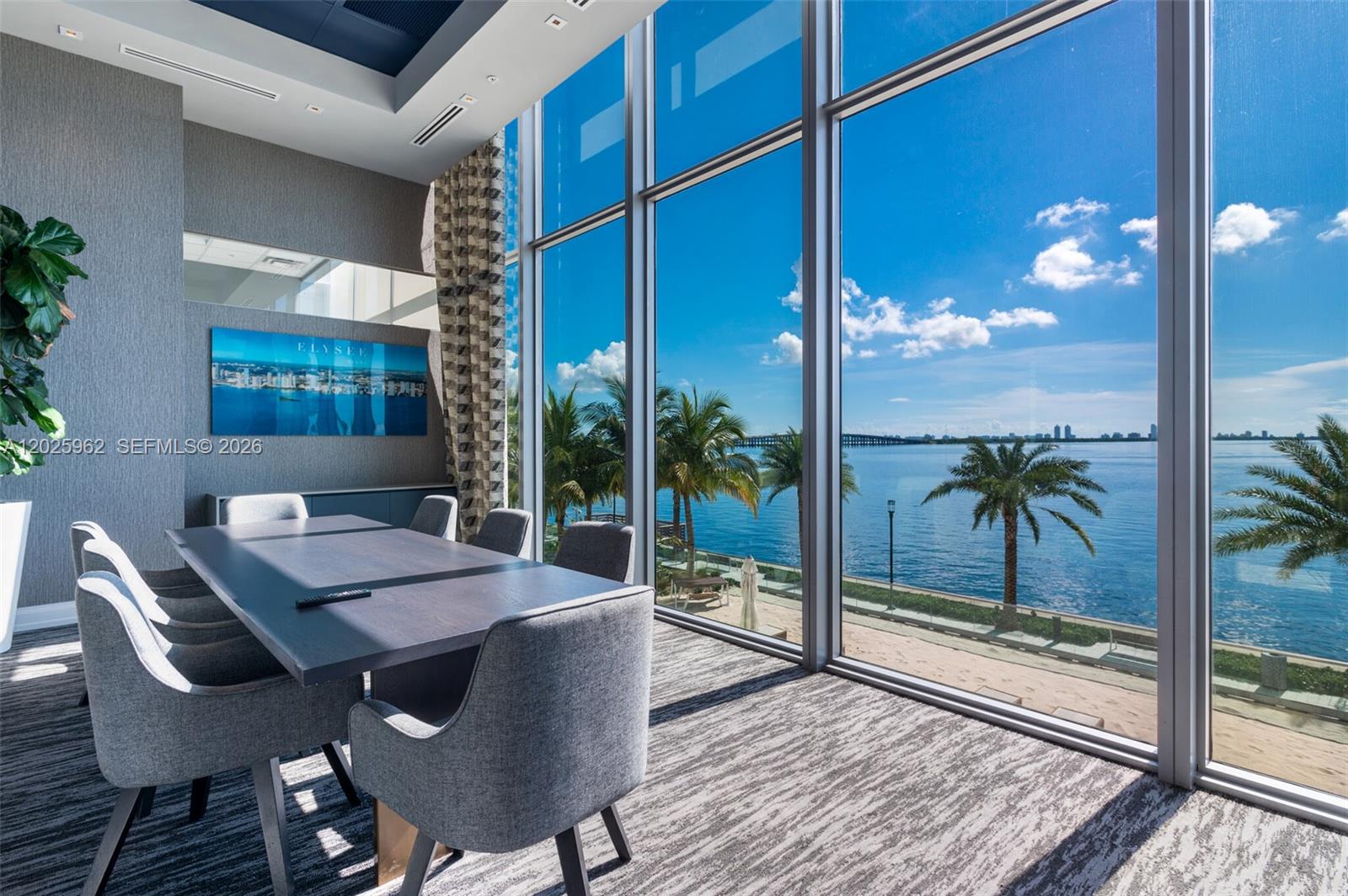A modern conference room features a dark table, gray chairs, and floor-to-ceiling waterfront windows — MIAMI, FL