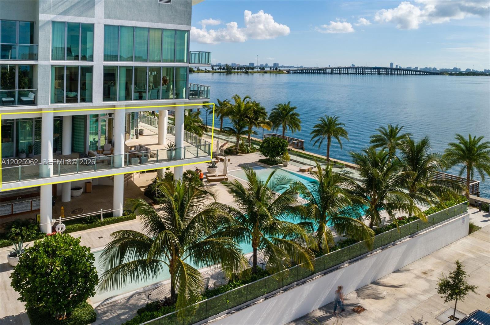 An elevated view shows a building balcony overlooking a swimming pool and a bay — MIAMI, FL