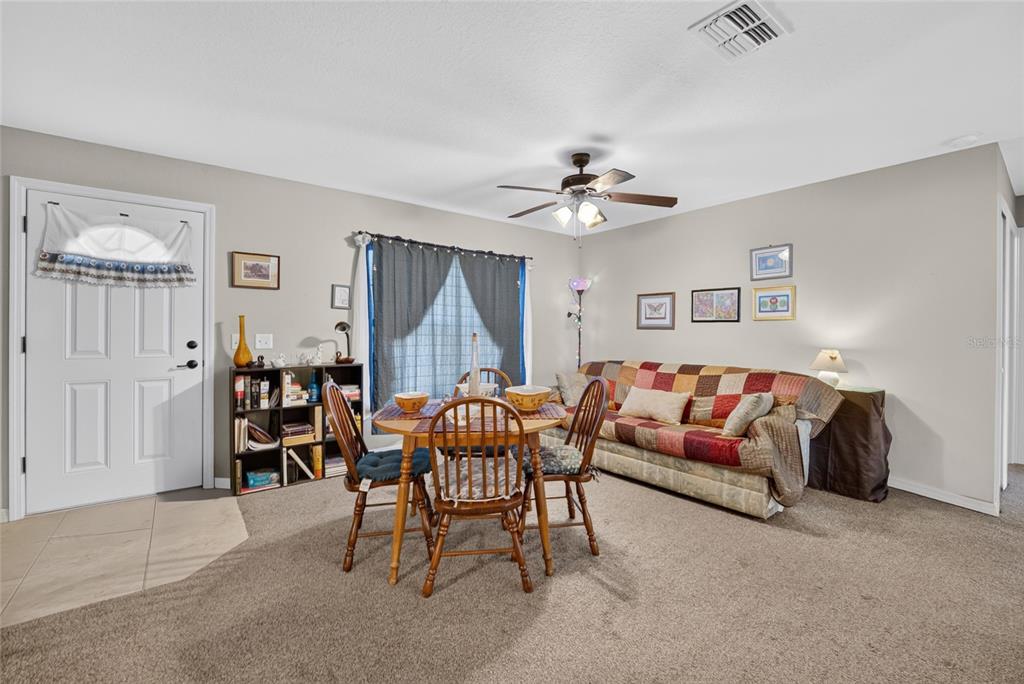 A living room with beige carpet, a patterned sofa, a bookshelf, and a ceiling fan — 13881 SW 33RD TERRACE, OCALA, FL