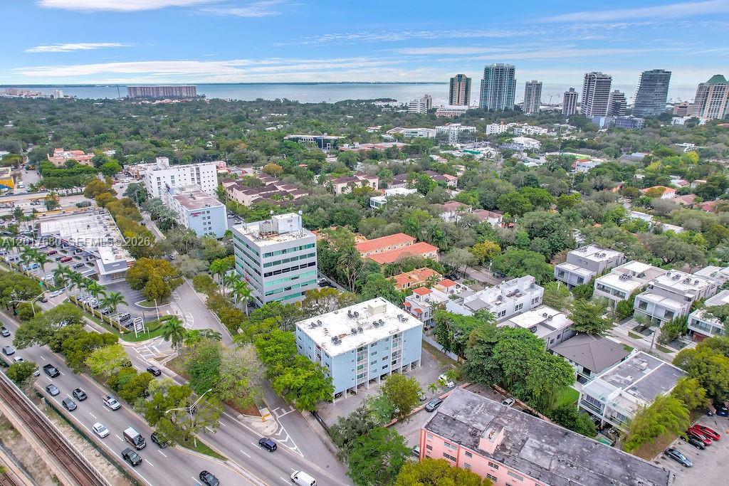 An aerial view shows a suburban neighborhood with mid-rise buildings, trees, and a distant bay — 2920 SW 28th Ter # 207, Miami FL 33133, MIAMI, FL