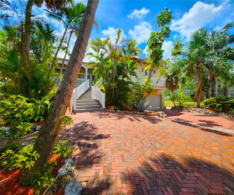 A brick driveway leads to a raised house with a white staircase and palm trees — 102 17TH STREET NE, BRADENTON, FL