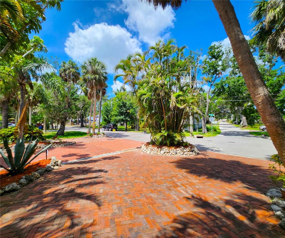A brick driveway leads toward a street intersection surrounded by palm trees and lush landscaping — 102 17TH STREET NE, BRADENTON, FL