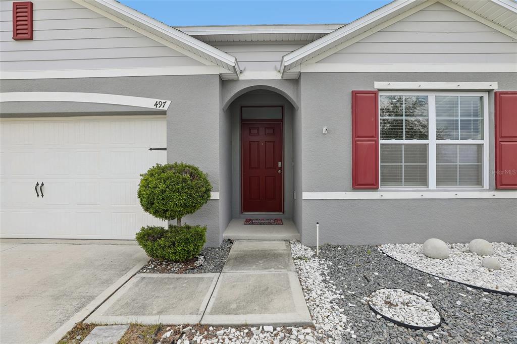The exterior of a gray house features a red front door, red shutters, and gravel landscaping — 497 NOBLE AVENUE, DAVENPORT, FL
