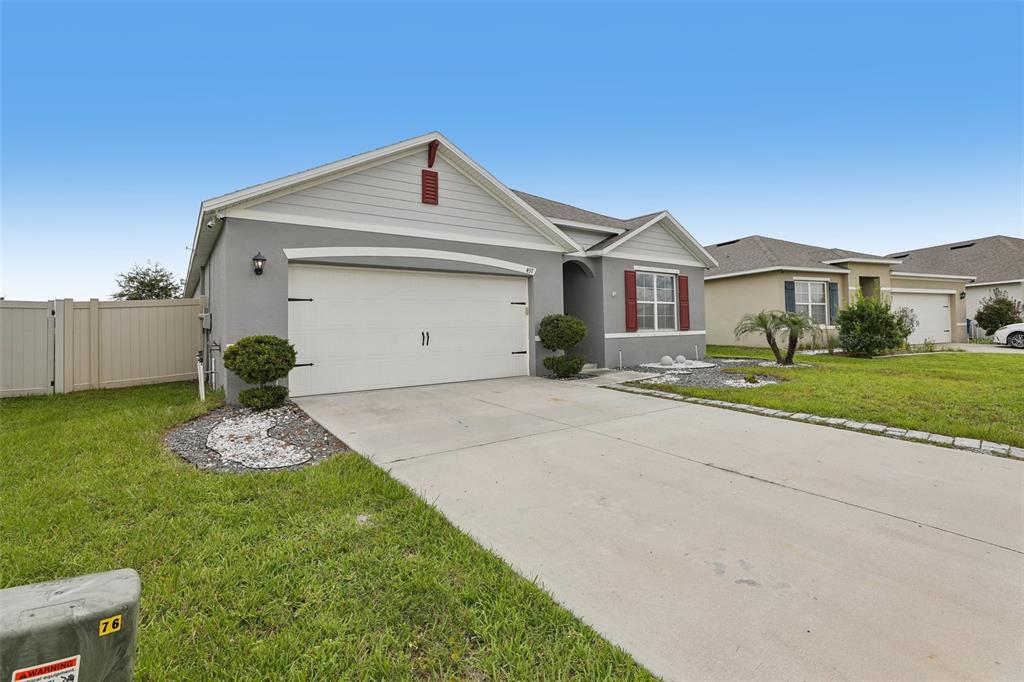 A single-story suburban house with a gray stucco exterior, white garage door, and red shutters — 497 NOBLE AVENUE, DAVENPORT, FL
