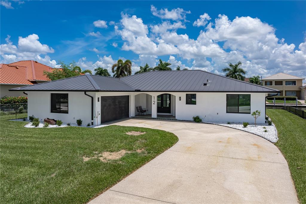 A single-story white house with a dark metal roof and a concrete driveway — 12 SABAL DRIVE, PUNTA GORDA, FL