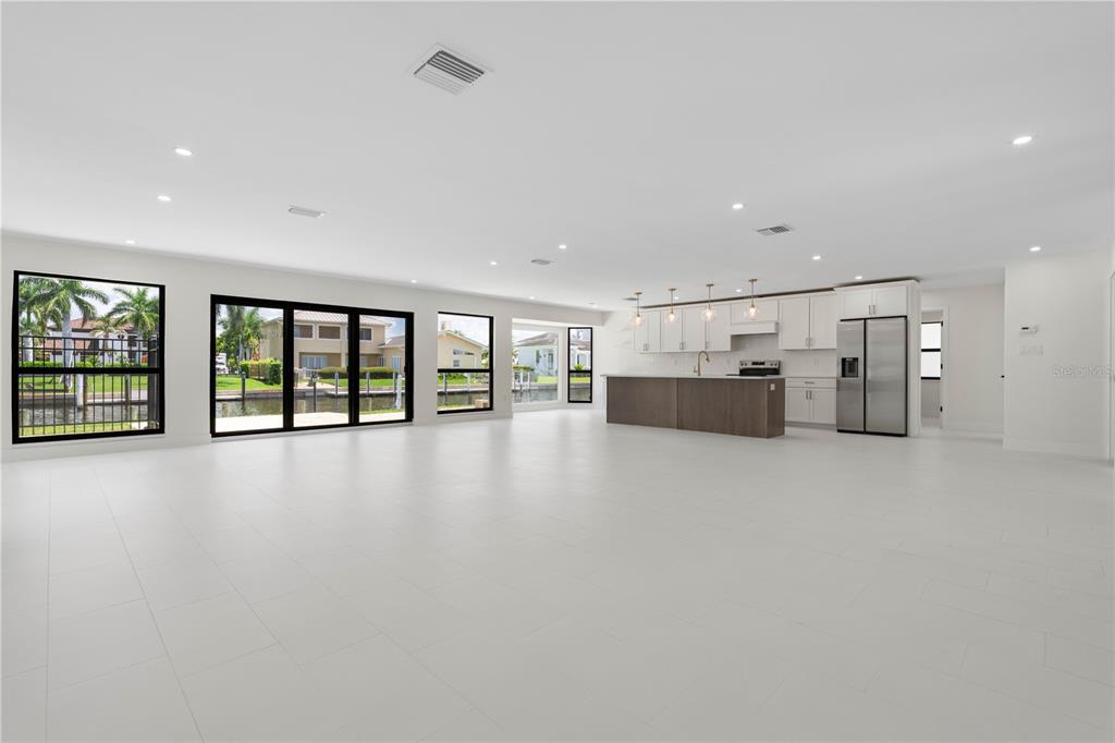 A spacious, open-concept room features white tile floors, a modern kitchen, and large windows — 12 SABAL DRIVE, PUNTA GORDA, FL