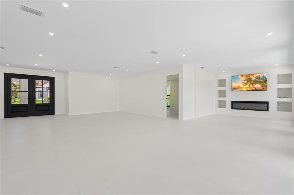 A bright, empty room with white tile floors, recessed lighting, double doors, and a fireplace — 12 SABAL DRIVE, PUNTA GORDA, FL