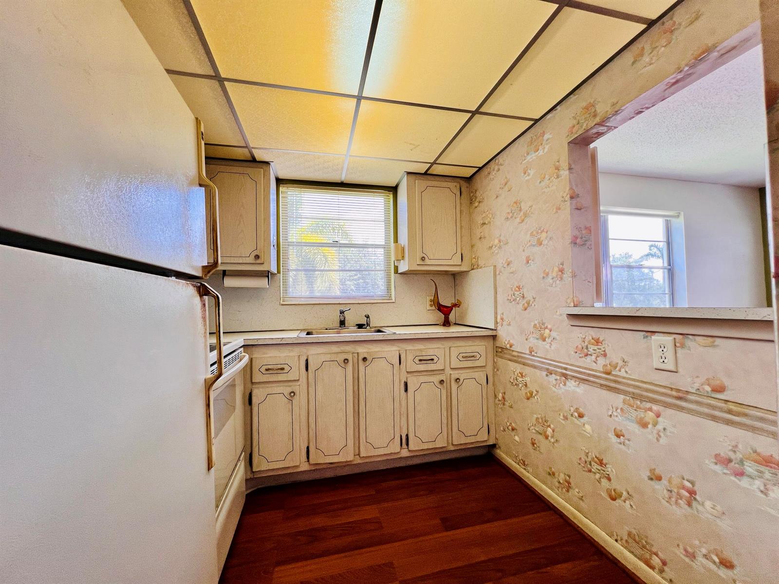 A kitchen features light-colored cabinets, floral wallpaper, a drop ceiling, and wood-look flooring — 339 Windsor O, West Palm Beach FL 33417, WEST PALM BEACH, FL