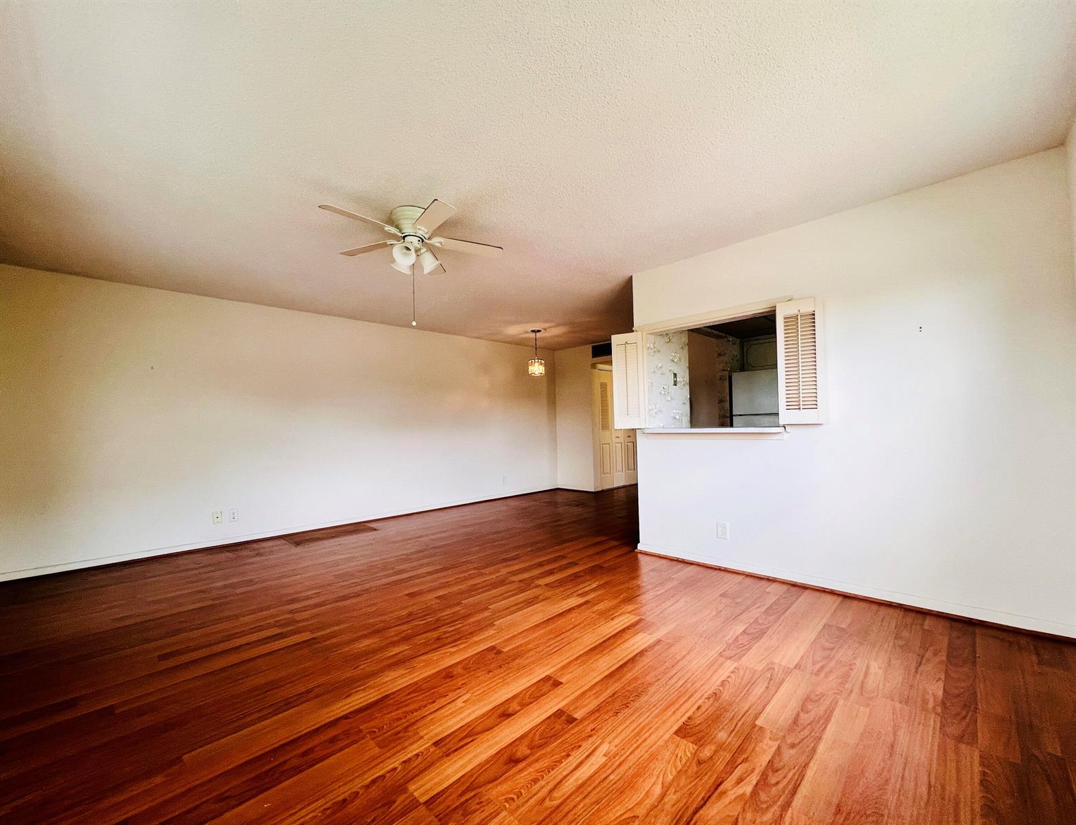 An empty living room with hardwood floors, a ceiling fan, and a kitchen pass-through window — 339 Windsor O, West Palm Beach FL 33417, WEST PALM BEACH, FL