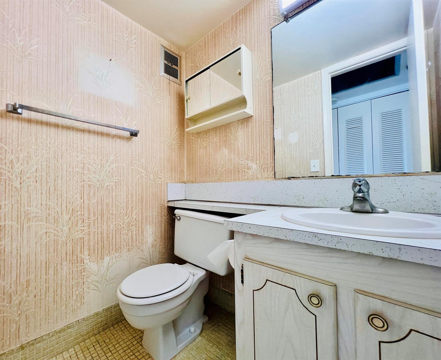 A bathroom features a vanity with a speckled countertop, a toilet, and patterned wallpaper — 339 Windsor O, West Palm Beach FL 33417, WEST PALM BEACH, FL