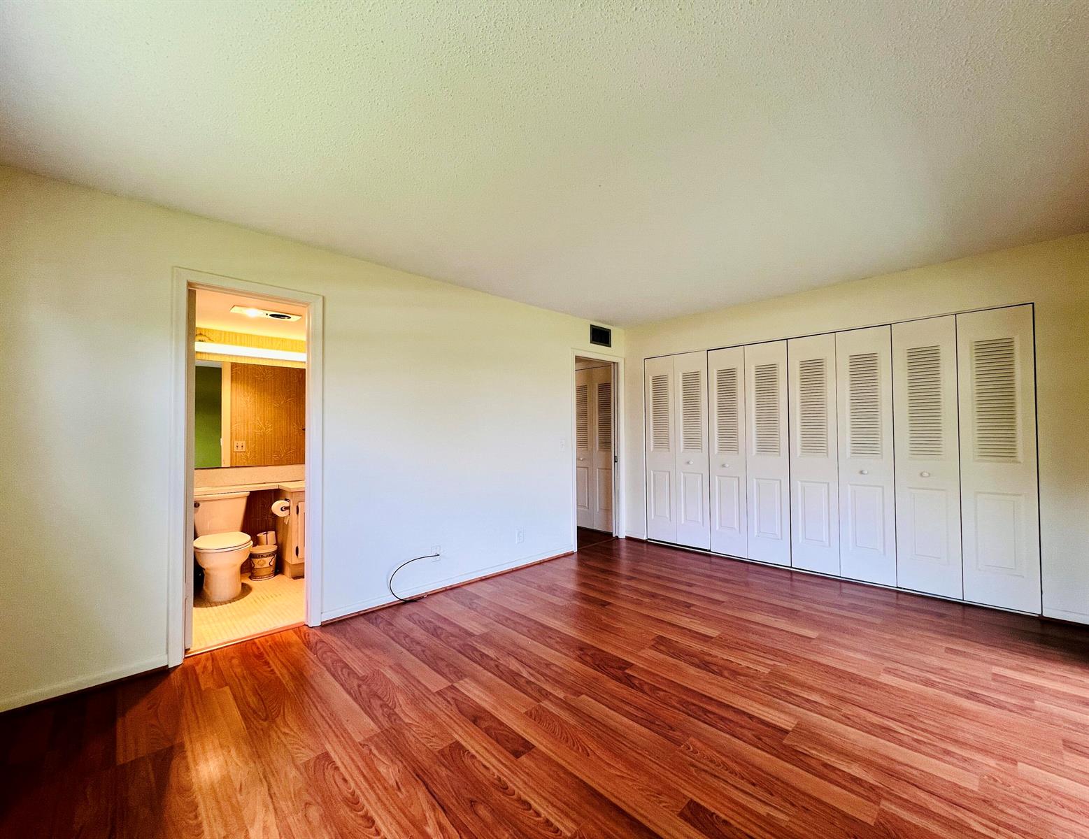 A bedroom with wood-look flooring, white walls, a bathroom entrance, and a wall of closets — 339 Windsor O, West Palm Beach FL 33417, WEST PALM BEACH, FL