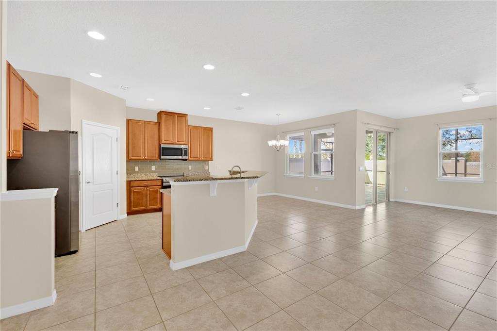 A kitchen with wood cabinets and a breakfast bar opens into a tiled living area — 244 WHIRLAWAY DRIVE, DAVENPORT, FL