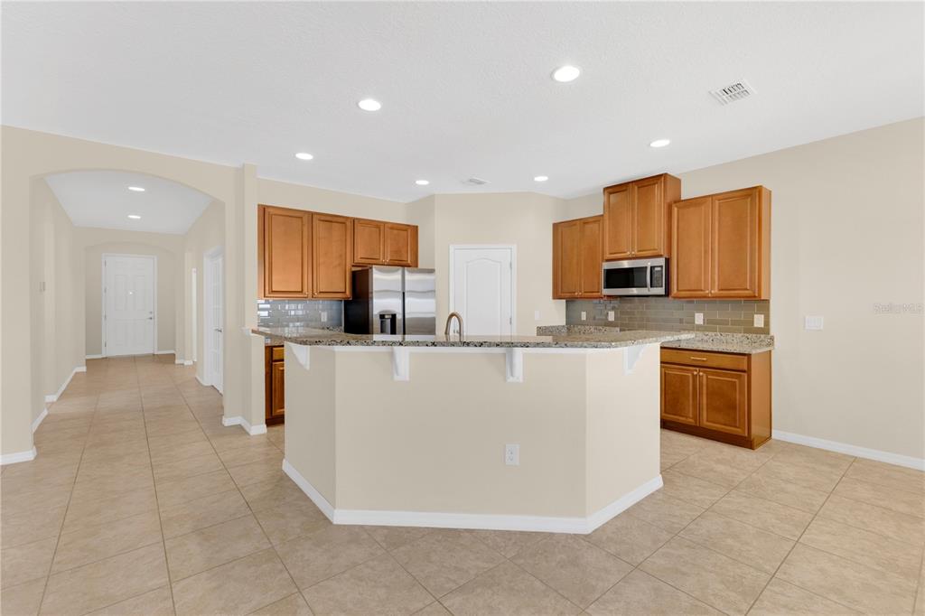 A kitchen features wood cabinets, granite countertops, a breakfast bar, and light-colored tile flooring — 244 WHIRLAWAY DRIVE, DAVENPORT, FL