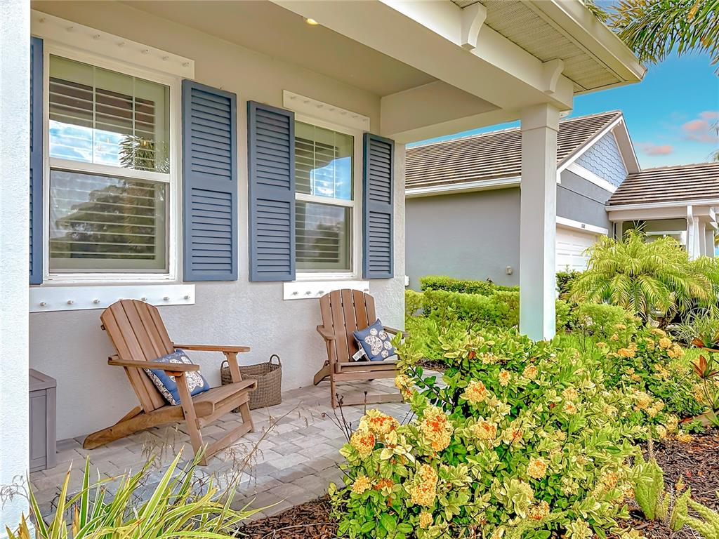 A covered front porch features two wooden Adirondack chairs and blue shutters on the windows — 18073 GRAND PROSPERITY DRIVE, VENICE, FL