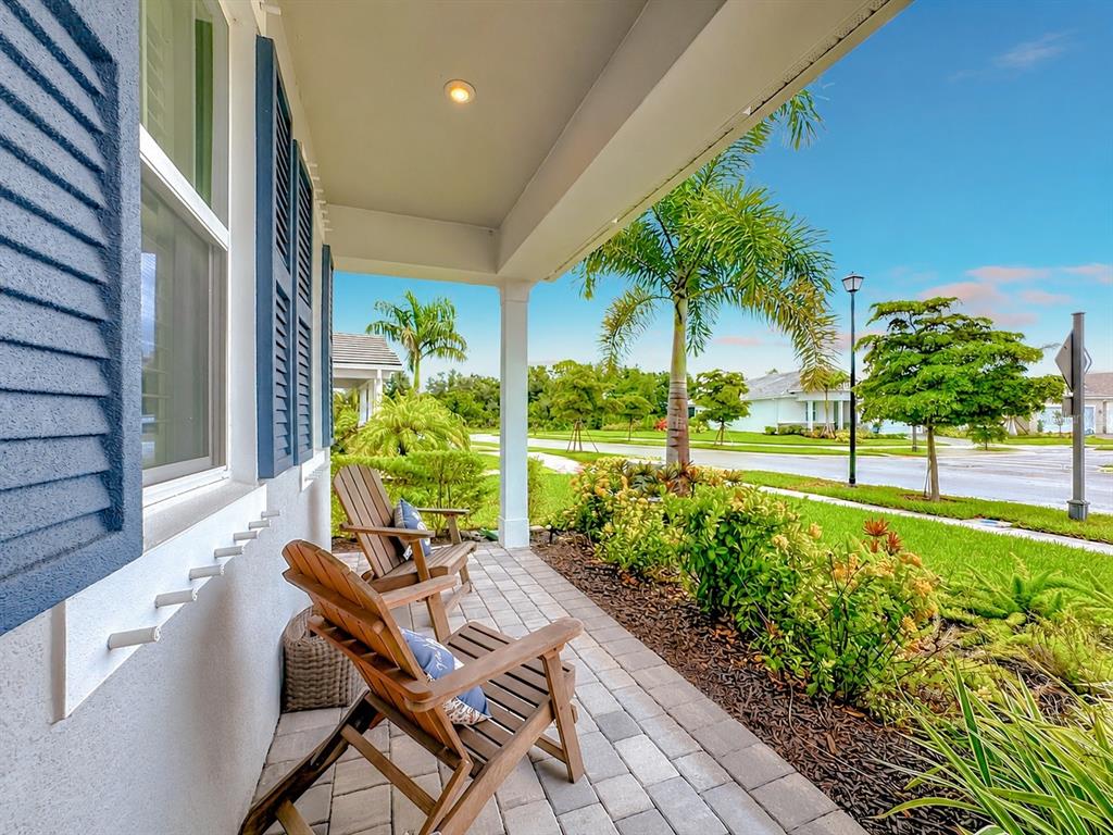 A covered front porch features two wooden chairs, blue shutters, and a view of landscaping — 18073 GRAND PROSPERITY DRIVE, VENICE, FL