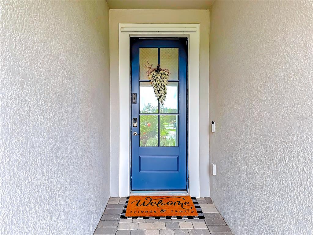 A blue front door with a decorative wreath sits at the end of a walkway — 18073 GRAND PROSPERITY DRIVE, VENICE, FL