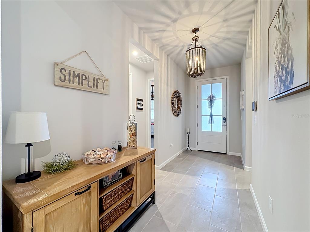 A bright entryway features a wooden console table, tile flooring, and a decorative beaded chandelier — 18073 GRAND PROSPERITY DRIVE, VENICE, FL