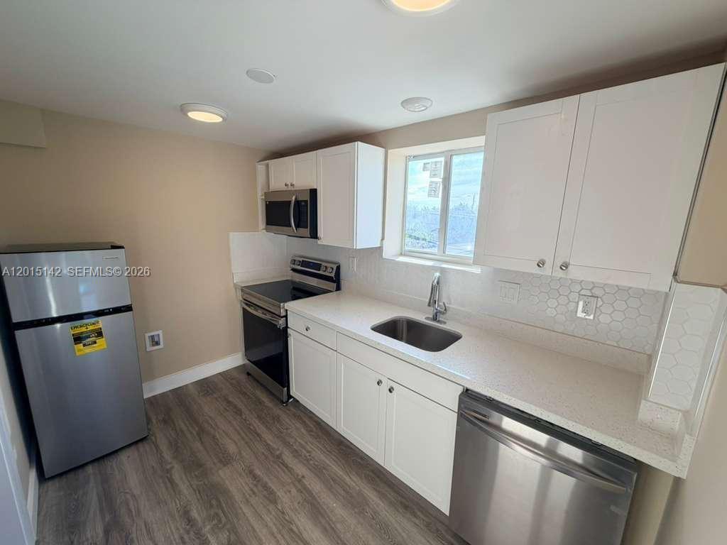 A kitchen features white cabinets, stainless steel appliances, a light countertop, and wood-look flooring — 943 79th Ter # 202, Miami Beach FL 33141, MIAMI BEACH, FL