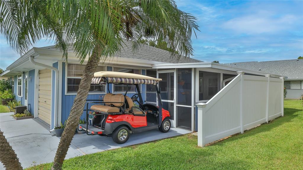 A red golf cart is parked on a concrete patio beside a blue house — 12 BOGEY CIRCLE, NEW SMYRNA BEACH, FL