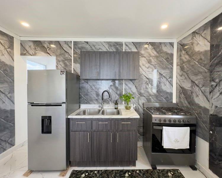 A kitchen features dark wood cabinets, a stainless steel refrigerator, a gas stove, and marble-patterned walls — Carr-10 E BO LOS CAÑOS CARR-10 R651 KM 10.5, ARECIBO, PR