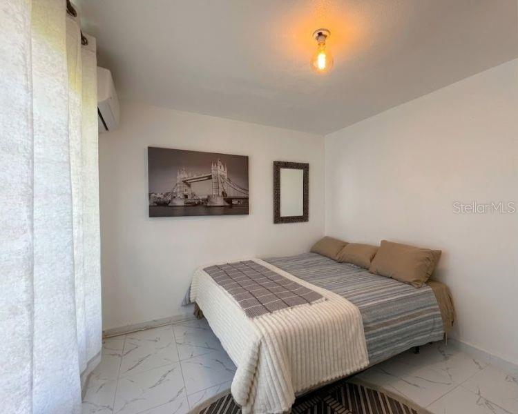 A bedroom with white walls, tile flooring, a bed with tan bedding, and wall art — Carr-10 E BO LOS CAÑOS CARR-10 R651 KM 10.5, ARECIBO, PR