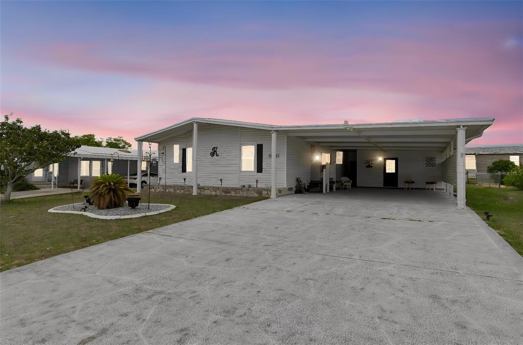 A single-story mobile home with a large concrete driveway and an attached carport at sunset — 14131 DELSILVER DRIVE, BROOKSVILLE, FL