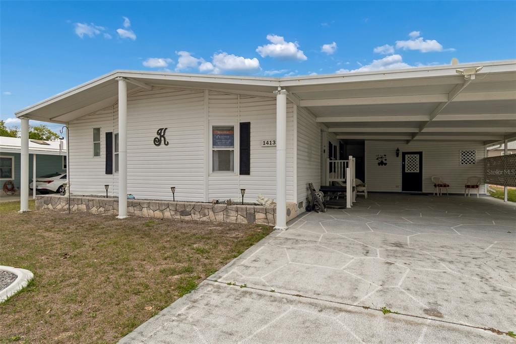 A white manufactured home features a stone-accented base, a large carport, and a concrete driveway — 14131 DELSILVER DRIVE, BROOKSVILLE, FL