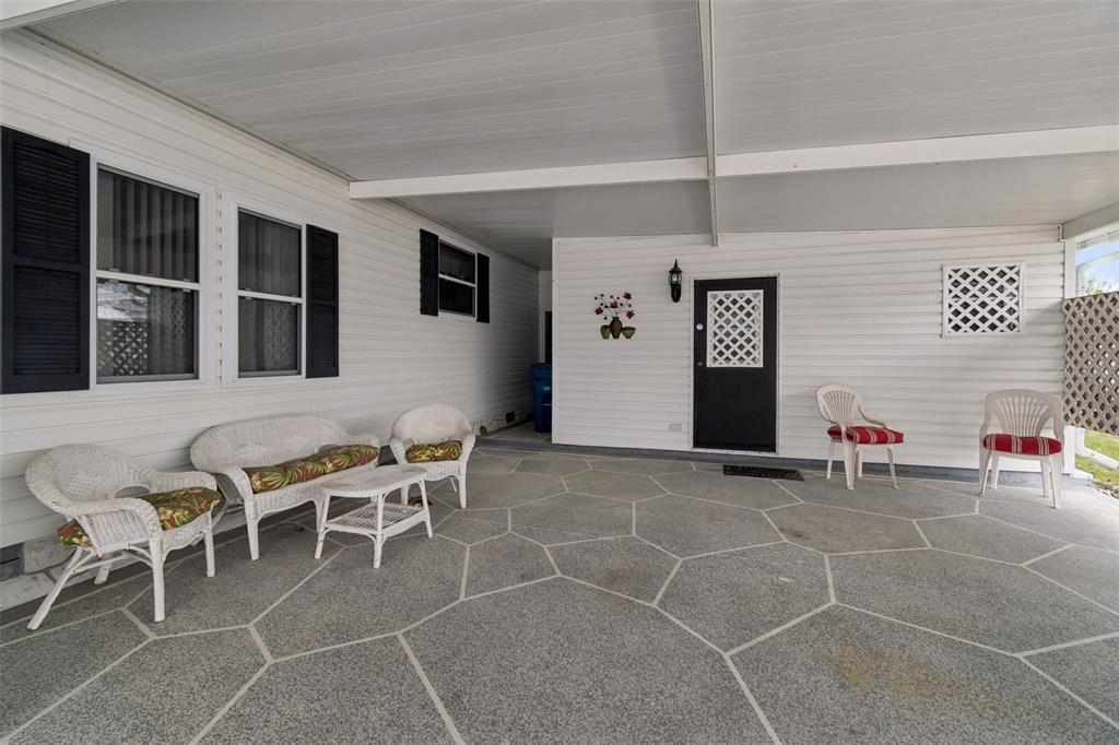 A covered patio features a patterned concrete floor, white siding, and several pieces of furniture — 14131 DELSILVER DRIVE, BROOKSVILLE, FL