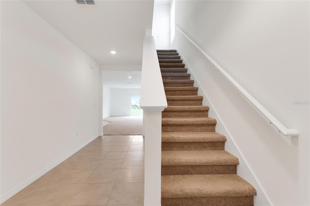 A staircase with brown carpet leads upward next to a tiled entryway and hallway — 1923 ELKRIDGE ST, DAVENPORT, FL