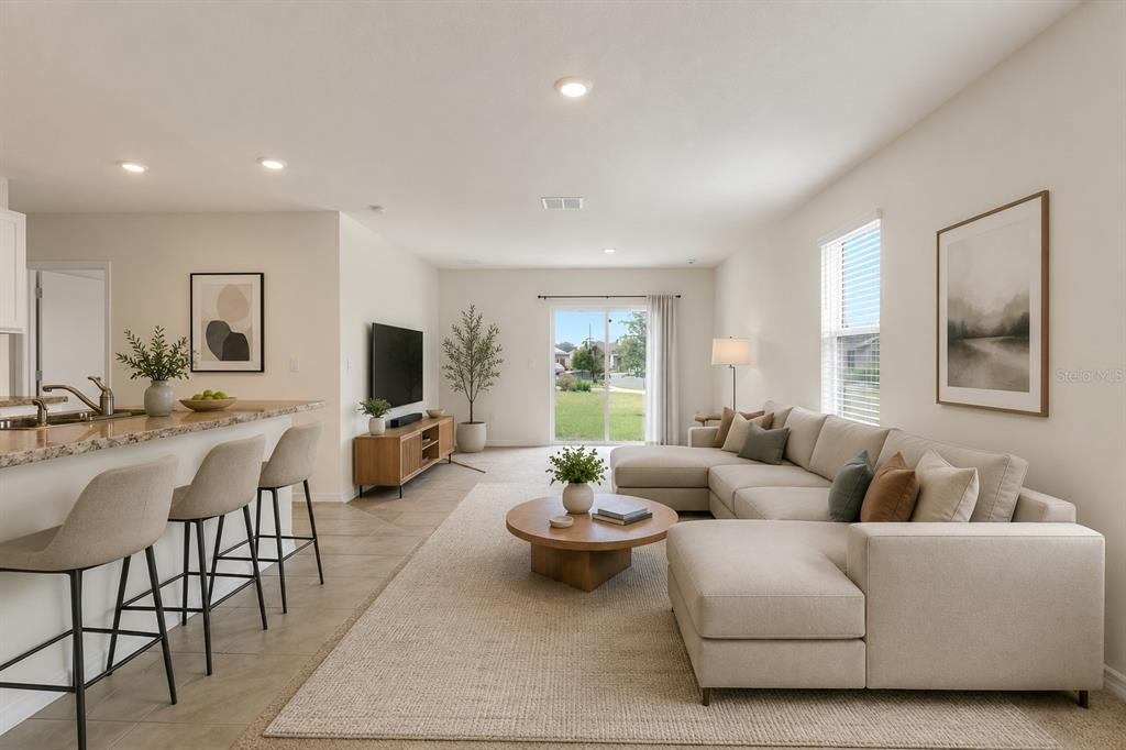 An open-concept living room features a sectional sofa, kitchen island with barstools, and sliding doors — 1923 ELKRIDGE ST, DAVENPORT, FL