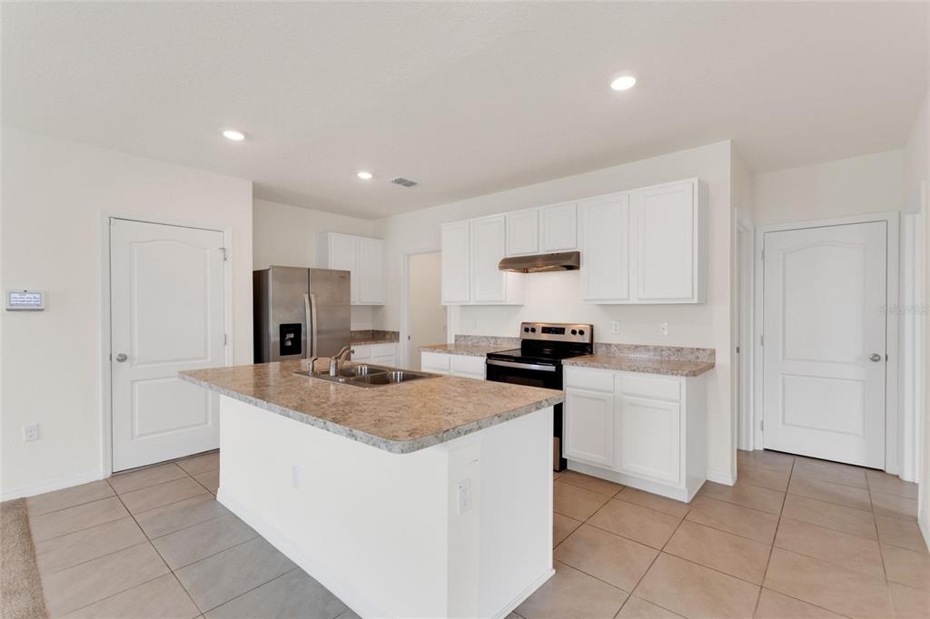 A kitchen with white cabinets, a granite-topped island, stainless steel appliances, and tiled flooring — 1923 ELKRIDGE ST, DAVENPORT, FL