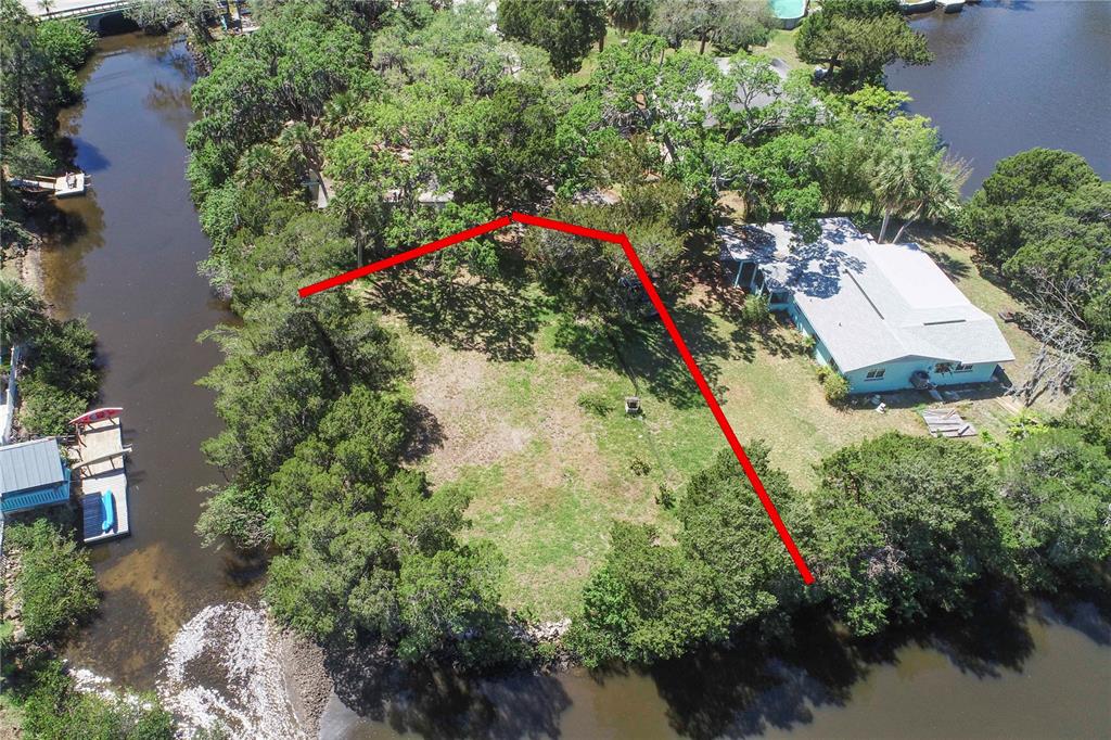 An aerial view shows a waterfront property with a house, a large yard, and trees — 5274 MILLER BAYOU DRIVE, PORT RICHEY, FL