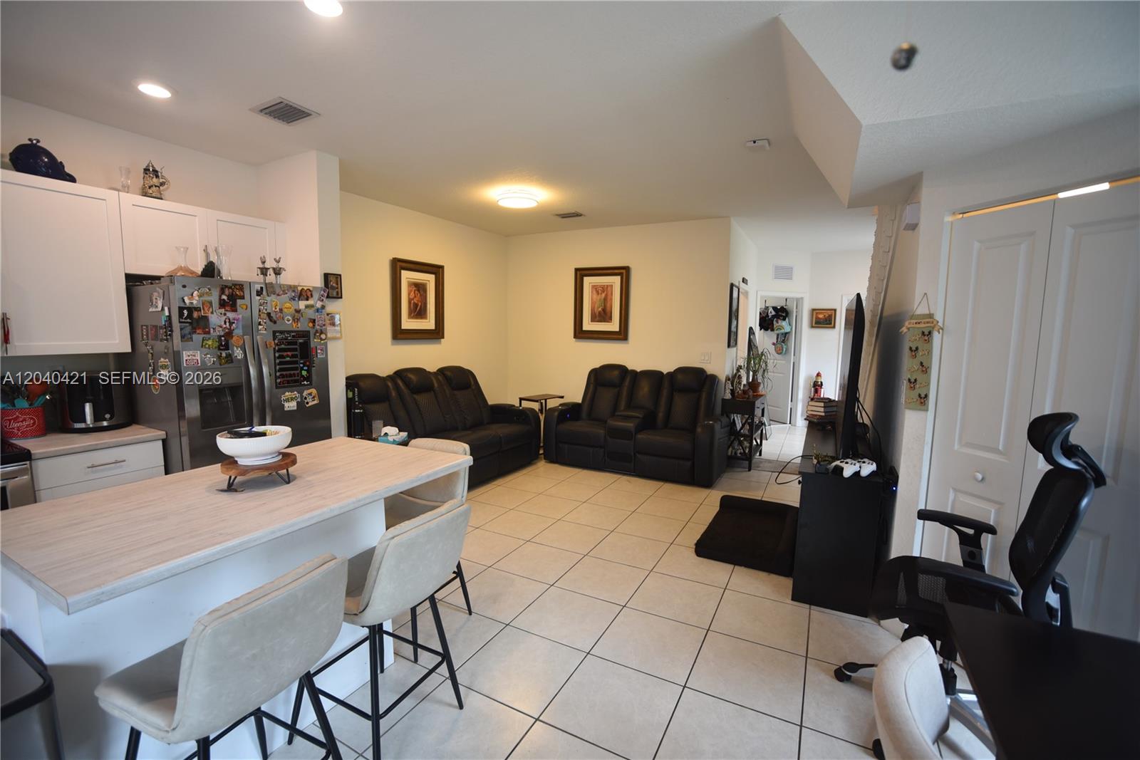 An open-concept kitchen and living area features white cabinets, tile flooring, and black leather seating — 21404 NE 3rd Path, Miami FL 33179, MIAMI, FL