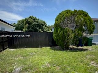 A black wooden fence separates a grassy backyard from a large, rounded evergreen tree — 863 NW 139th St, Miami FL 33168, MIAMI, FL