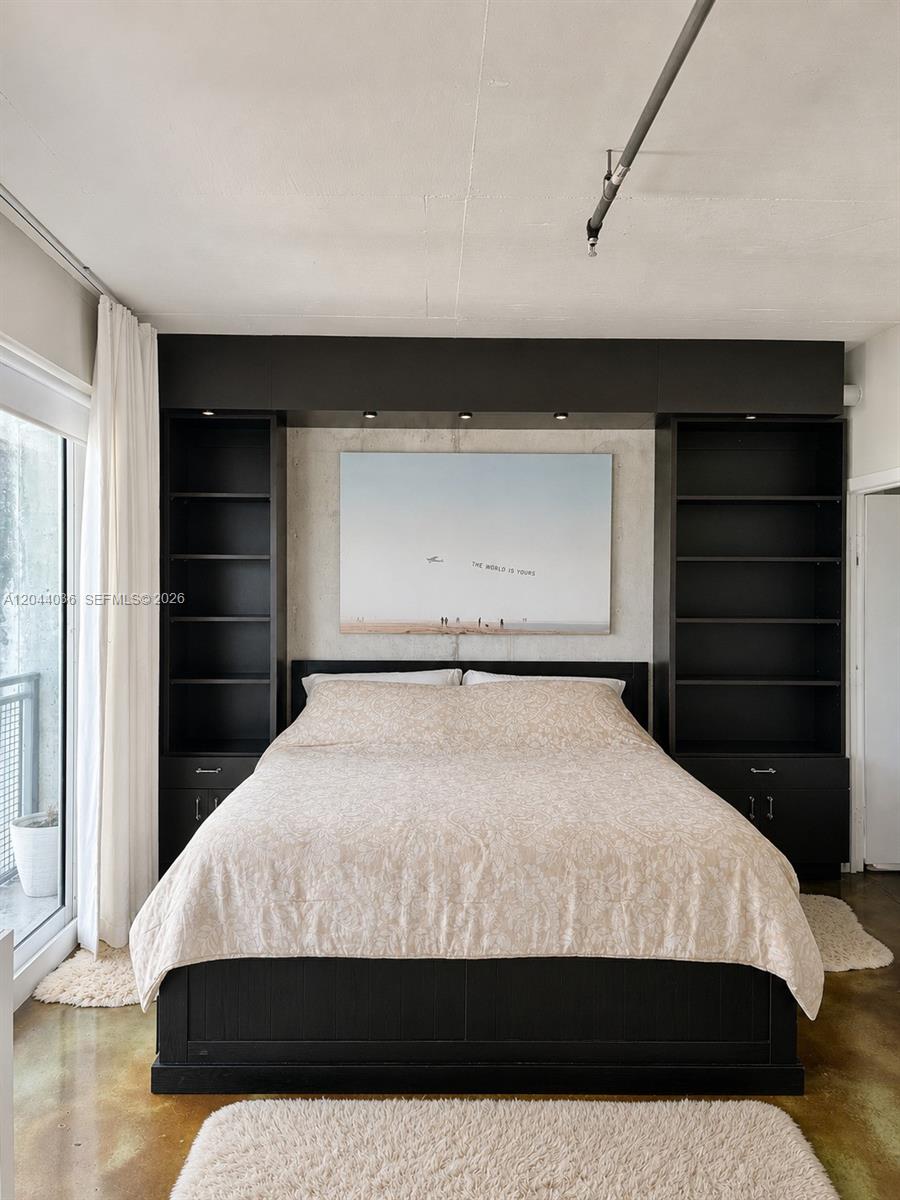 A bedroom features a bed centered between two tall black shelving units against a concrete wall — 455 NE 25th St # 806, Miami FL 33137, MIAMI, FL