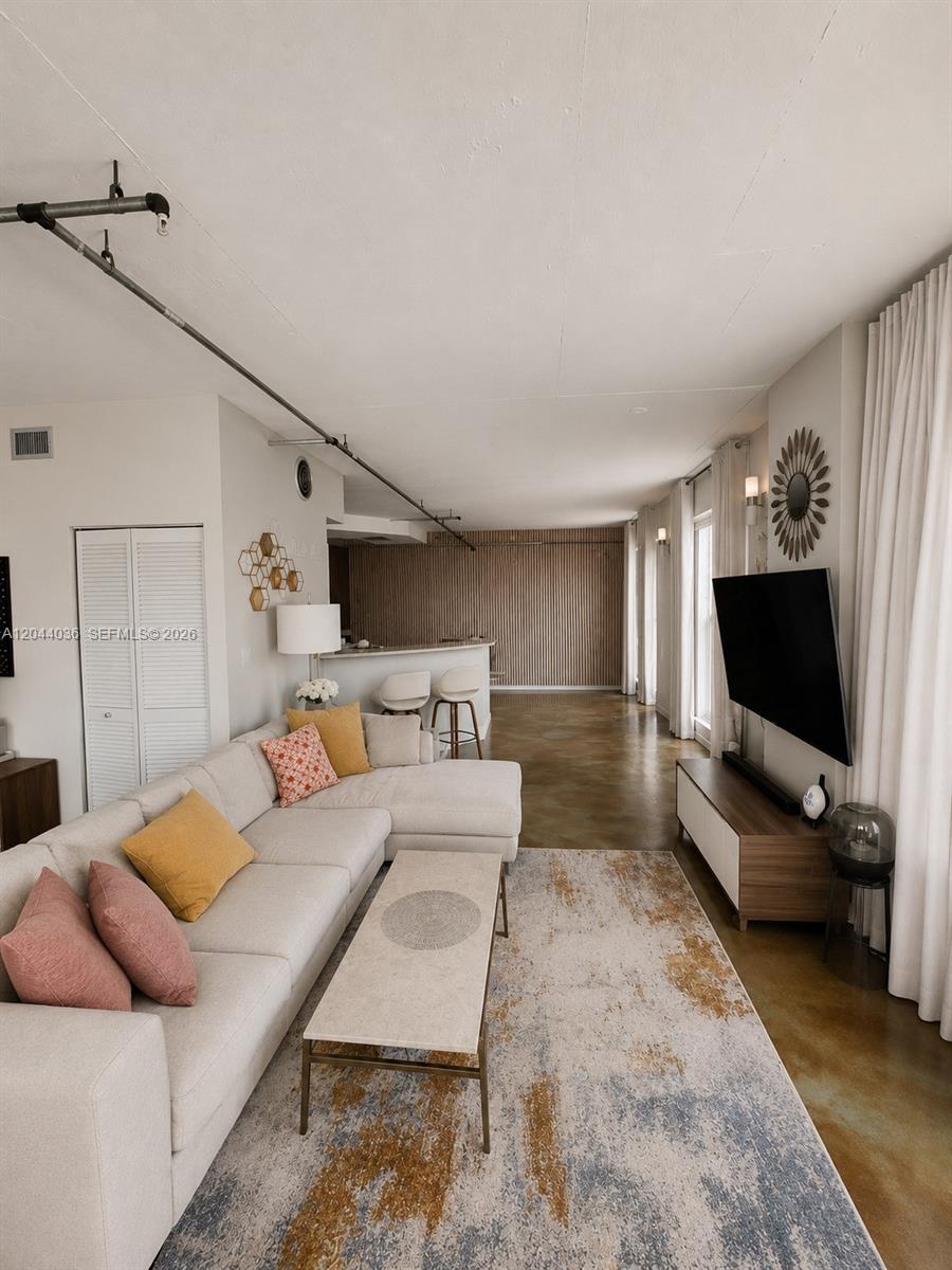 A living room features a sectional sofa, a television, and exposed industrial ceiling pipes — 455 NE 25th St # 806, Miami FL 33137, MIAMI, FL